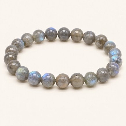 Bracelet en labradorite à perles rondes de 8 mm, grises avec des reflets bleutés et verdâtres, présenté sur fond beige clair.
