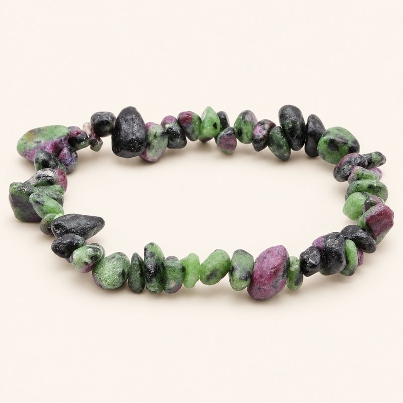 Bracelet baroque en rubis-zoïsite aux pierres polies vertes, noires et rose violacé, présenté sur fond beige clair. Bracelet baroque en rubis-zoïsite aux pierres polies vertes, noires et rose violacé, présenté sur fond beige clair.