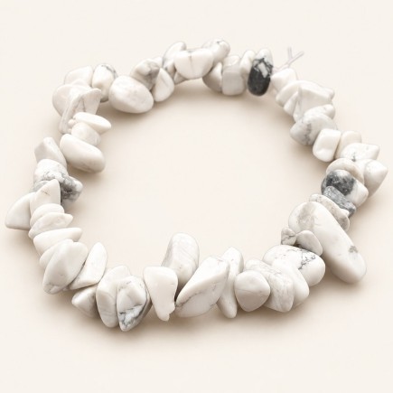 Bracelet baroque en howlite aux pierres polies blanches à ivoire, parcourues de veinures grises, présenté sur fond beige clair.