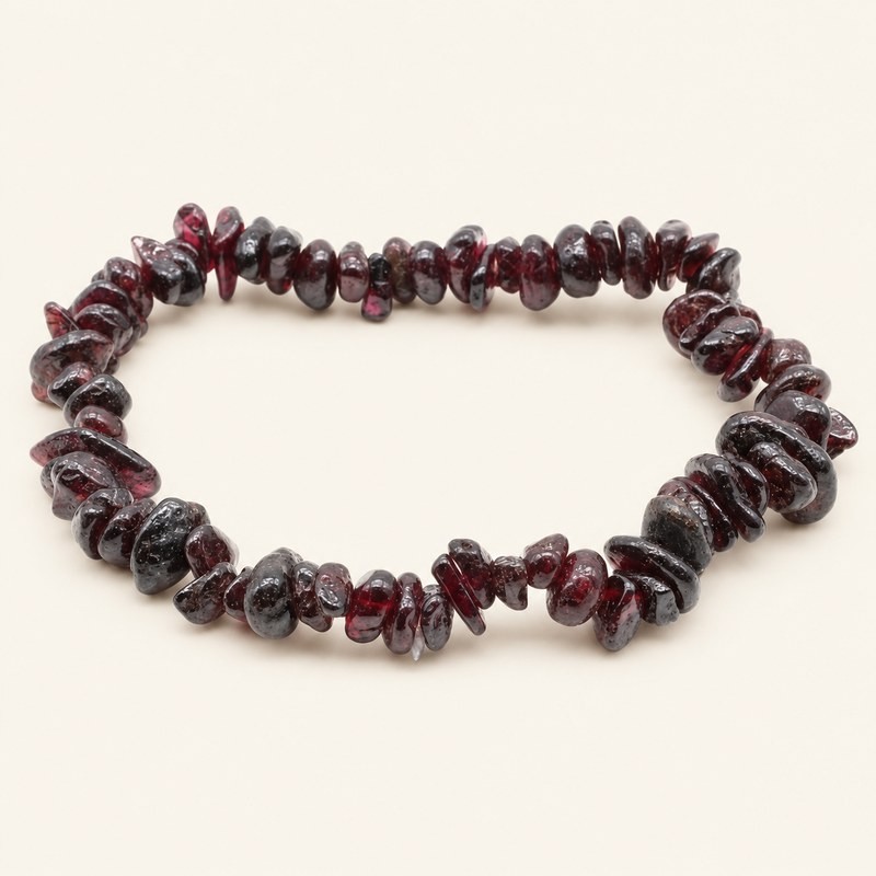 Bracelet baroque en grenat aux pierres chips rouge sombre et bordeaux, présenté sur fond beige. Bracelet baroque en grenat aux pierres chips rouge sombre et bordeaux, présenté sur fond beige.