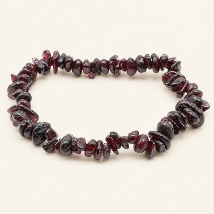 Bracelet baroque en grenat aux pierres chips rouge sombre et bordeaux, présenté sur fond beige.