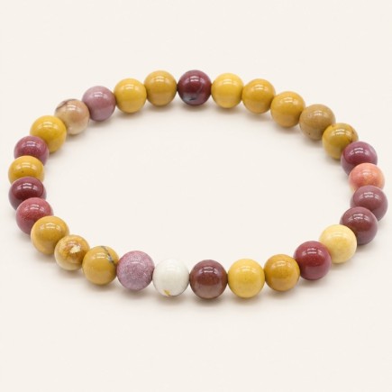 Bracelet en jaspe mokaïte, perles rondes de 8 mm aux nuances jaune ocre, bordeaux, rose et crème, sur fond beige.