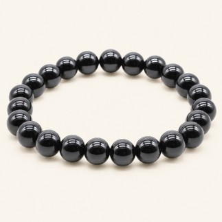 Bracelet en onyx noir du Brésil, perles rondes polies de 8 mm à la finition brillante, sur fond beige.
