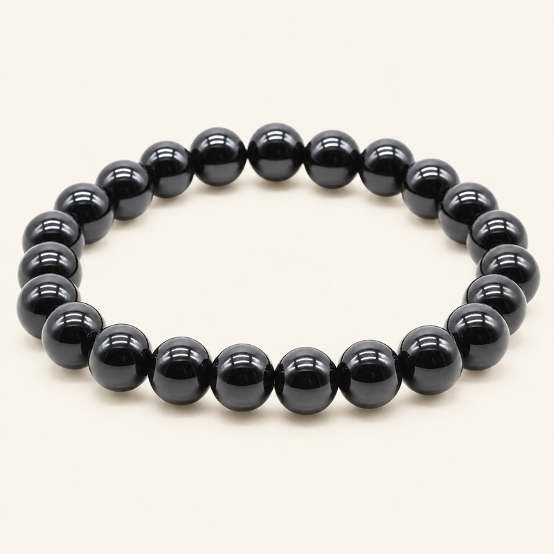 Bracelet en onyx noir du Brésil, perles rondes polies de 8 mm à la finition brillante, sur fond beige. Bracelet en onyx noir du Brésil, perles rondes polies de 8 mm à la finition brillante, sur fond beige.