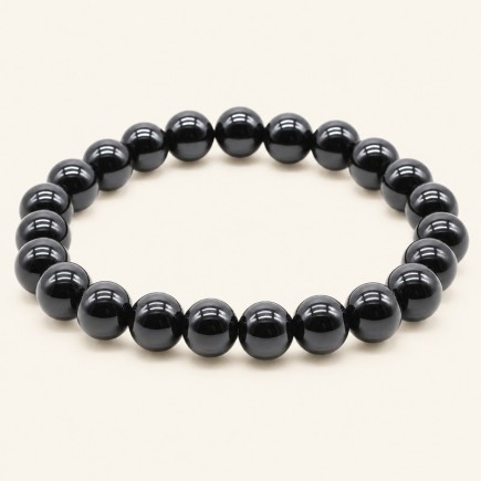 Bracelet en onyx noir du Brésil, perles rondes polies de 8 mm à la finition brillante, sur fond beige.